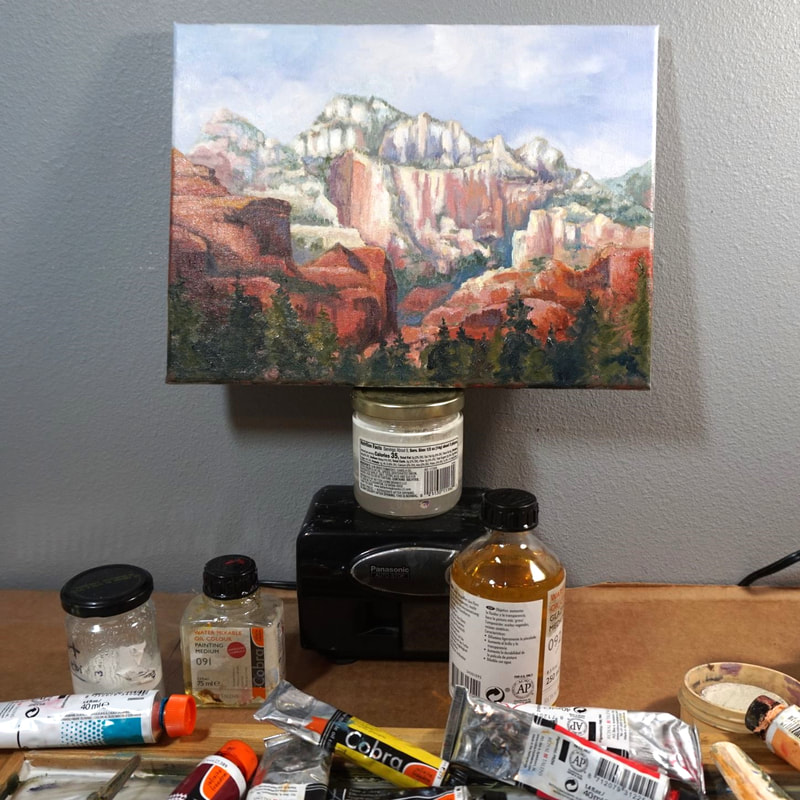 Studio picture of a small painting of Sedona.  Bottles and paint tubes are in front of it.  
