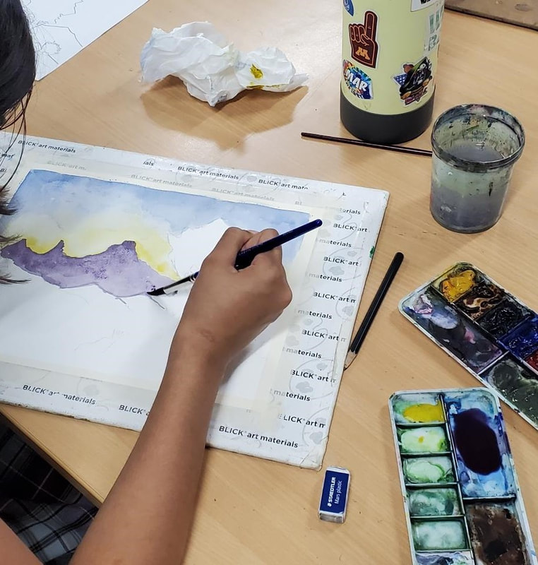 Student painting mountains in watercolor paint.  